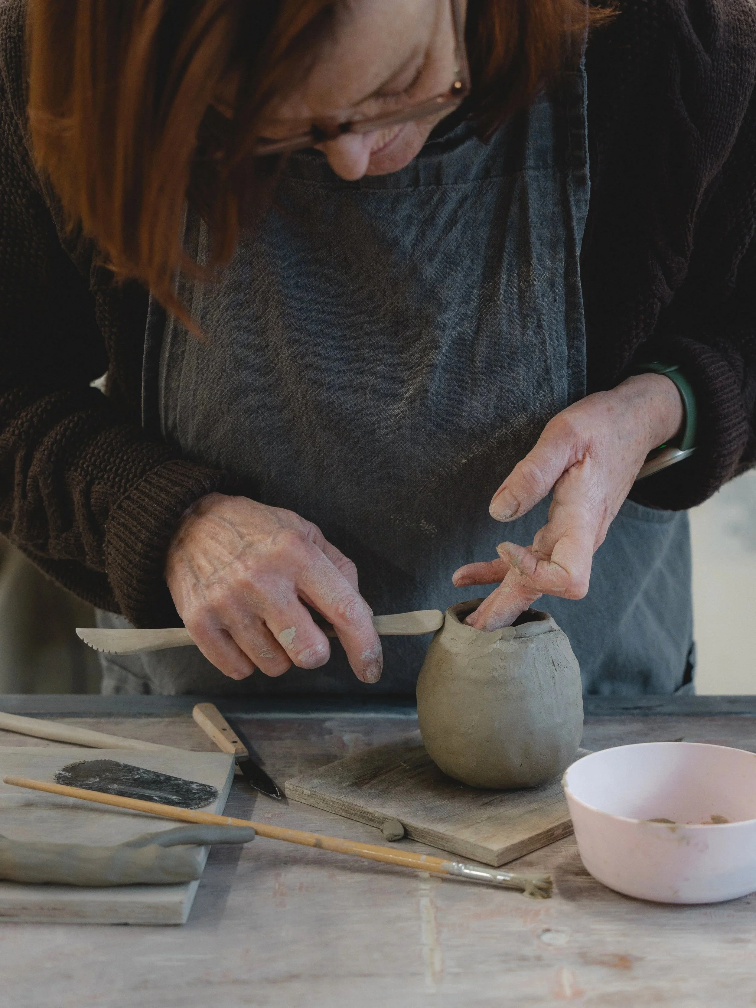 A person working on a ceramic pottery sculpture, shaping the clay with their hands and using a sculpting tool.