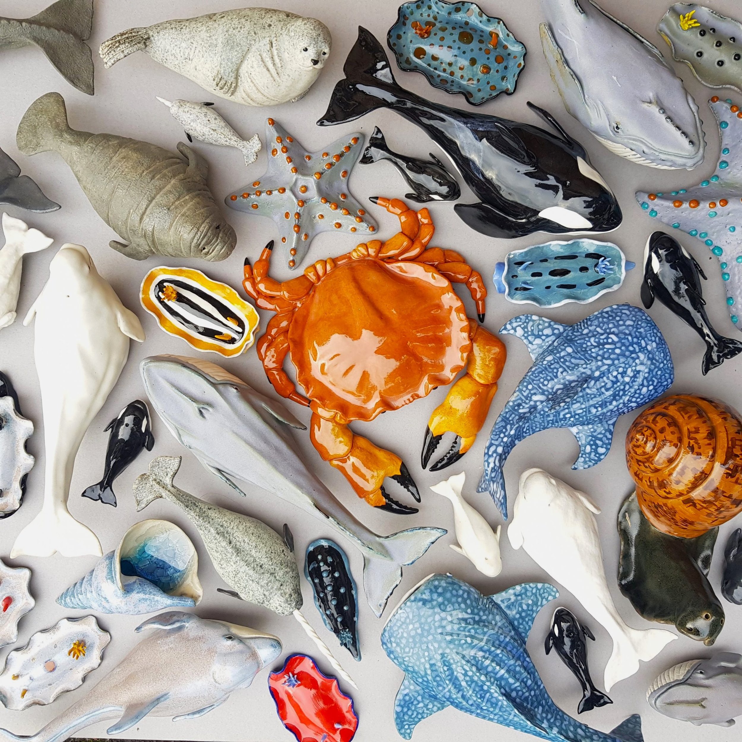 Collection of ceramic marine life sculptures, including fish, a crab, a starfish, a whale, a seahorse, and other sea creatures, glazed in various vibrant colors and patterns.