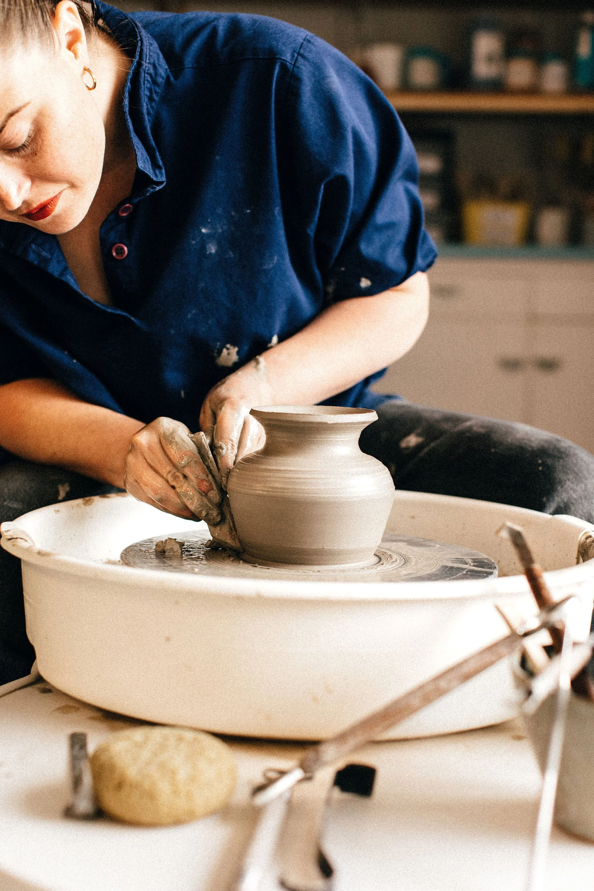 A person shaping a ceramic vase on a pottery wheel in a workshop.