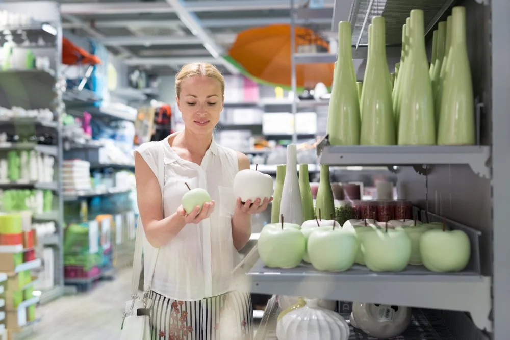 Woman shopping for green apples and green vases in a home goods store.