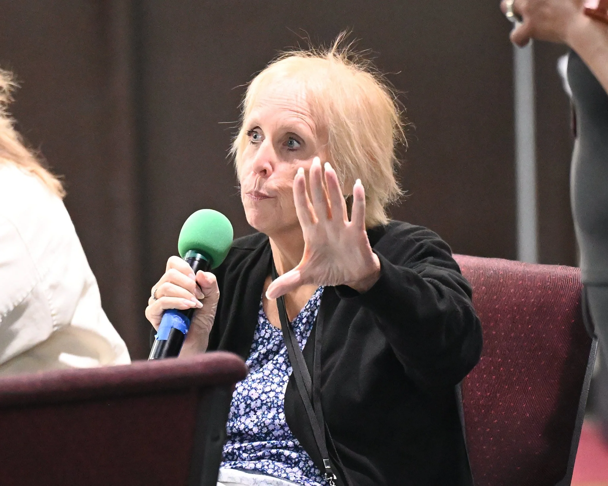 A woman with blonde hair and blue eyes holding a green microphone and speaking in a discussion.
