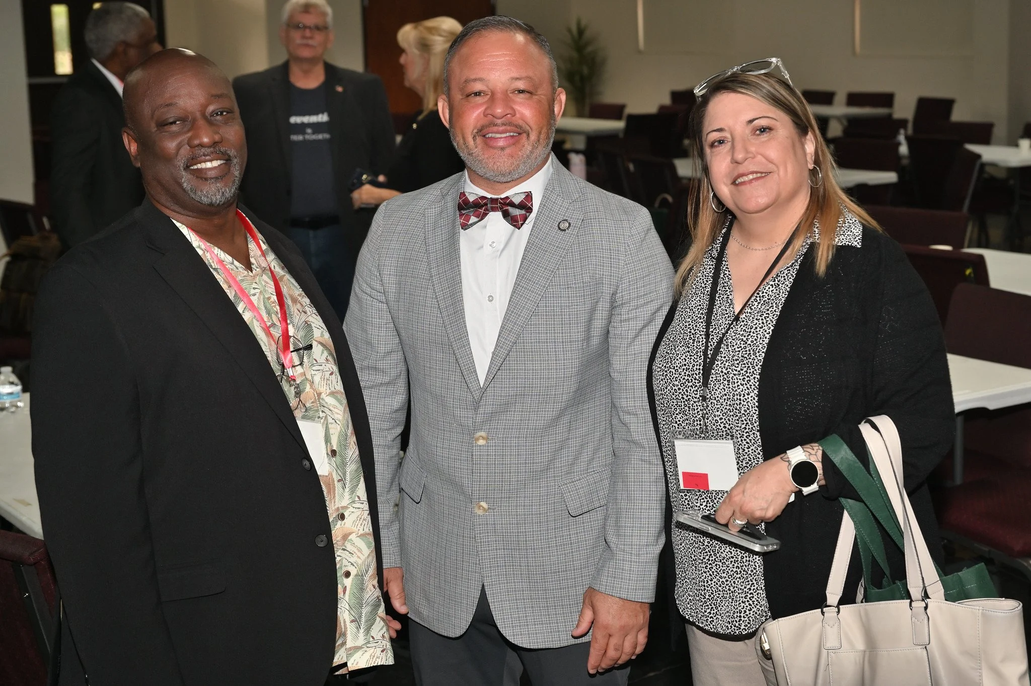 Three people at a professional event posing for a photo. The man on the left is wearing a black blazer with a patterned shirt and has a gray beard. The man in the middle has gray hair, a gray beard, and is wearing a gray checkered blazer with a white