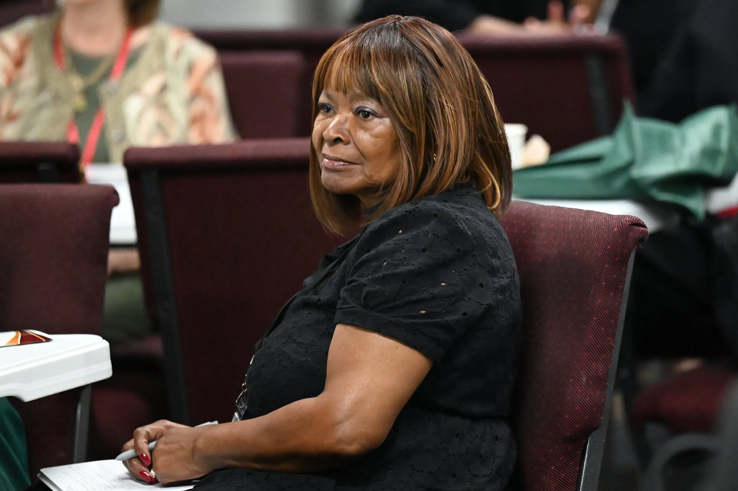 A woman with brown hair and a black lace top sitting at a conference table in a meeting room.