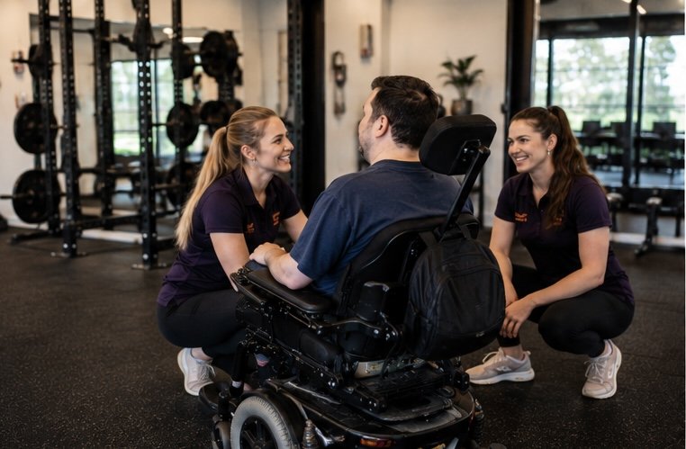 A man in a wheelchair talking with two female trainers in a gym.
