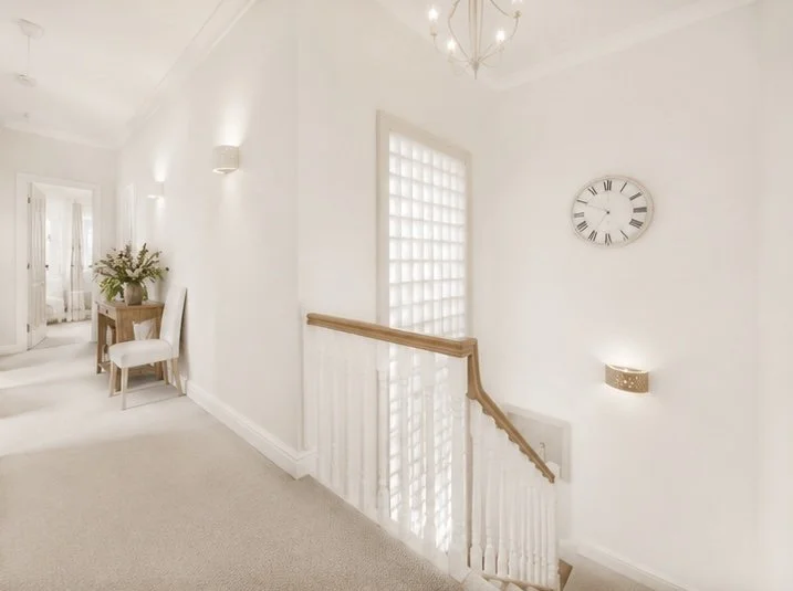 Bright white hallway with a staircase, glass block window, wall clock, and a small wall light beside the staircase.