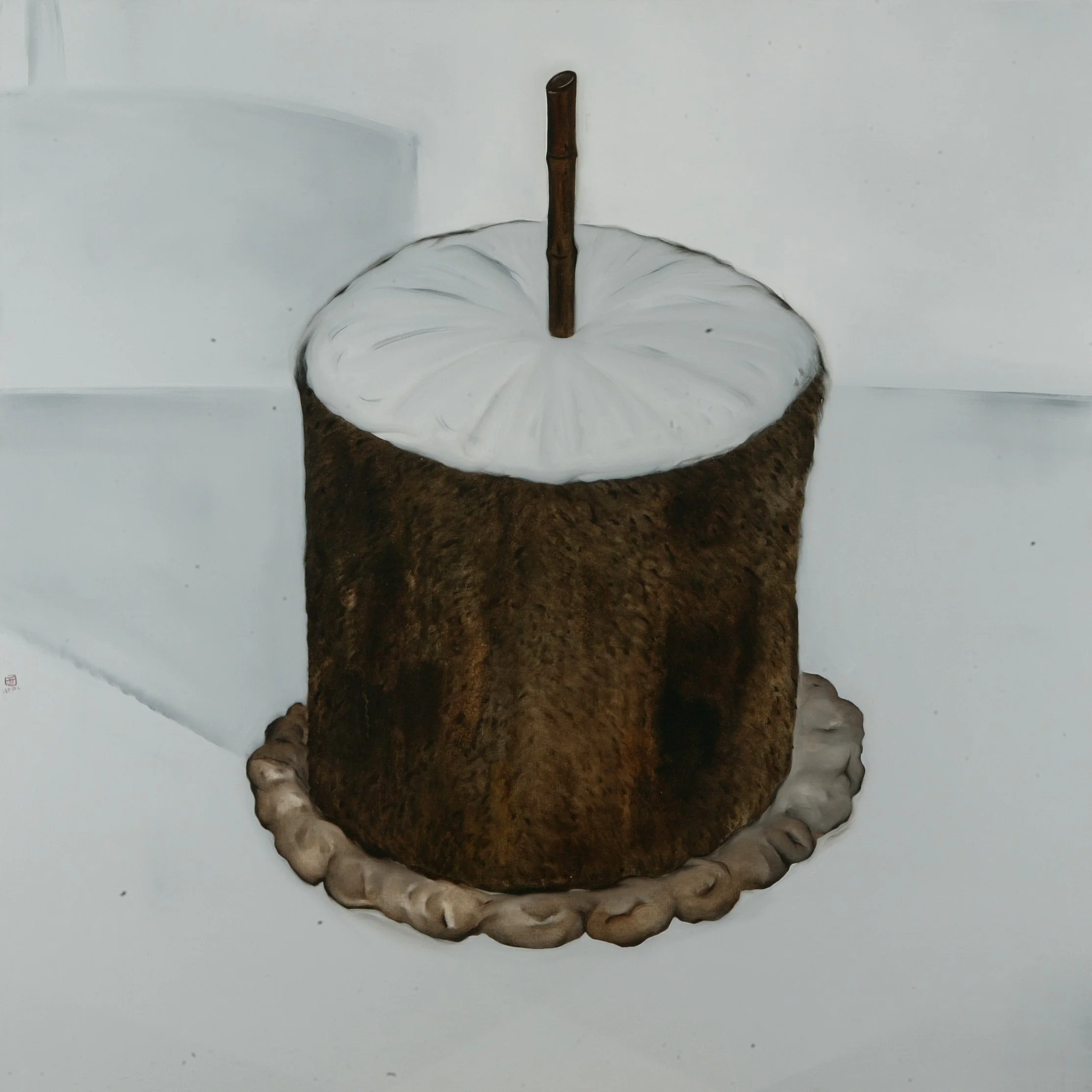 A brown pastry with a white icing drizzle on top, shaped into a ring with a chocolate stick in the center, placed on a white surface.