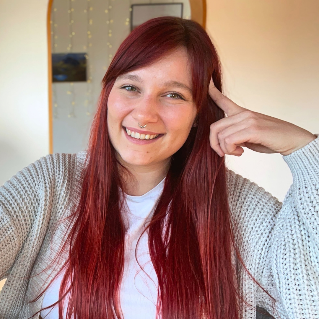 Pixel art avatar of Kathrin: A woman with light skin and red hair holding a coffee cup and wearing pink headphones. Morphs into a real life photo of Kathrin upon hovering.