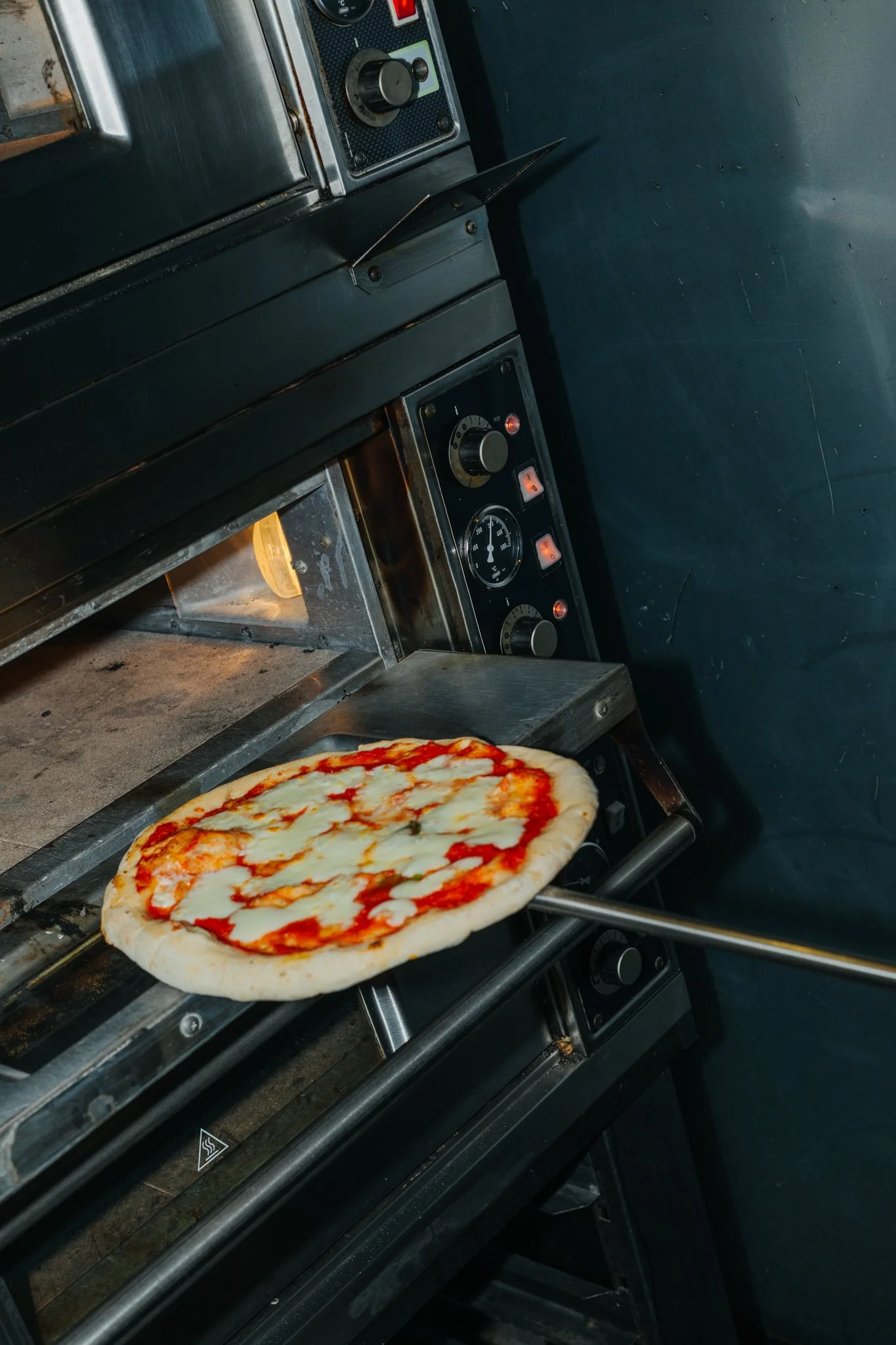 A pizza with melted cheese and tomato sauce being cooked on a conveyor oven line.