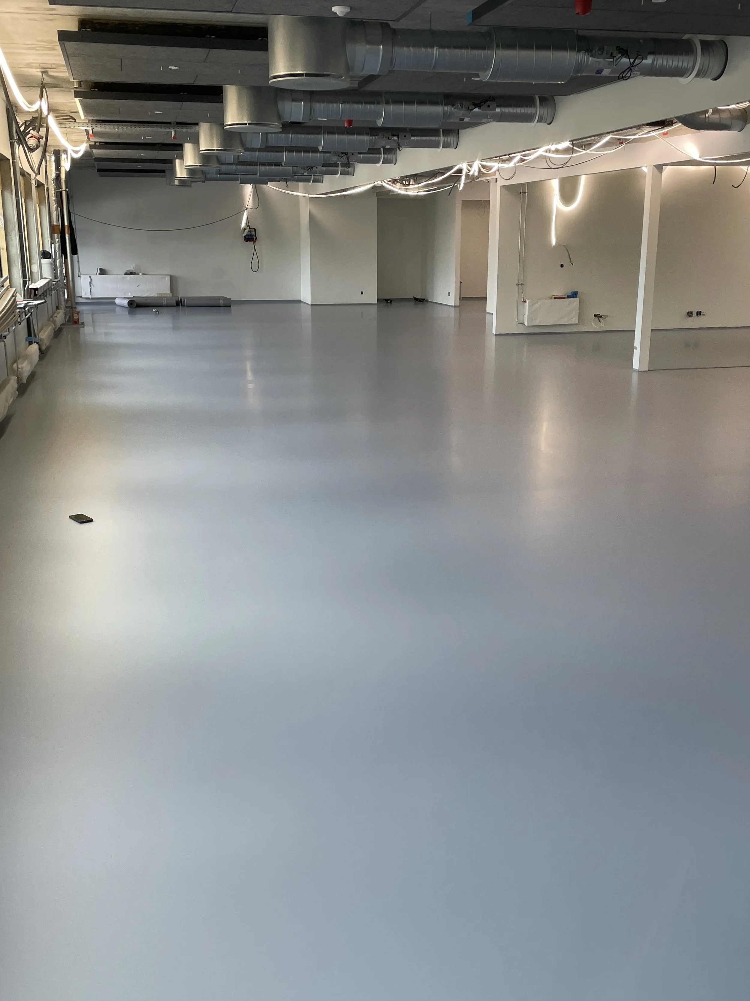 Room under konstruktion med synlige ventilationsrør, hvide vægge og gulv, samt nogle elektriske installationer.