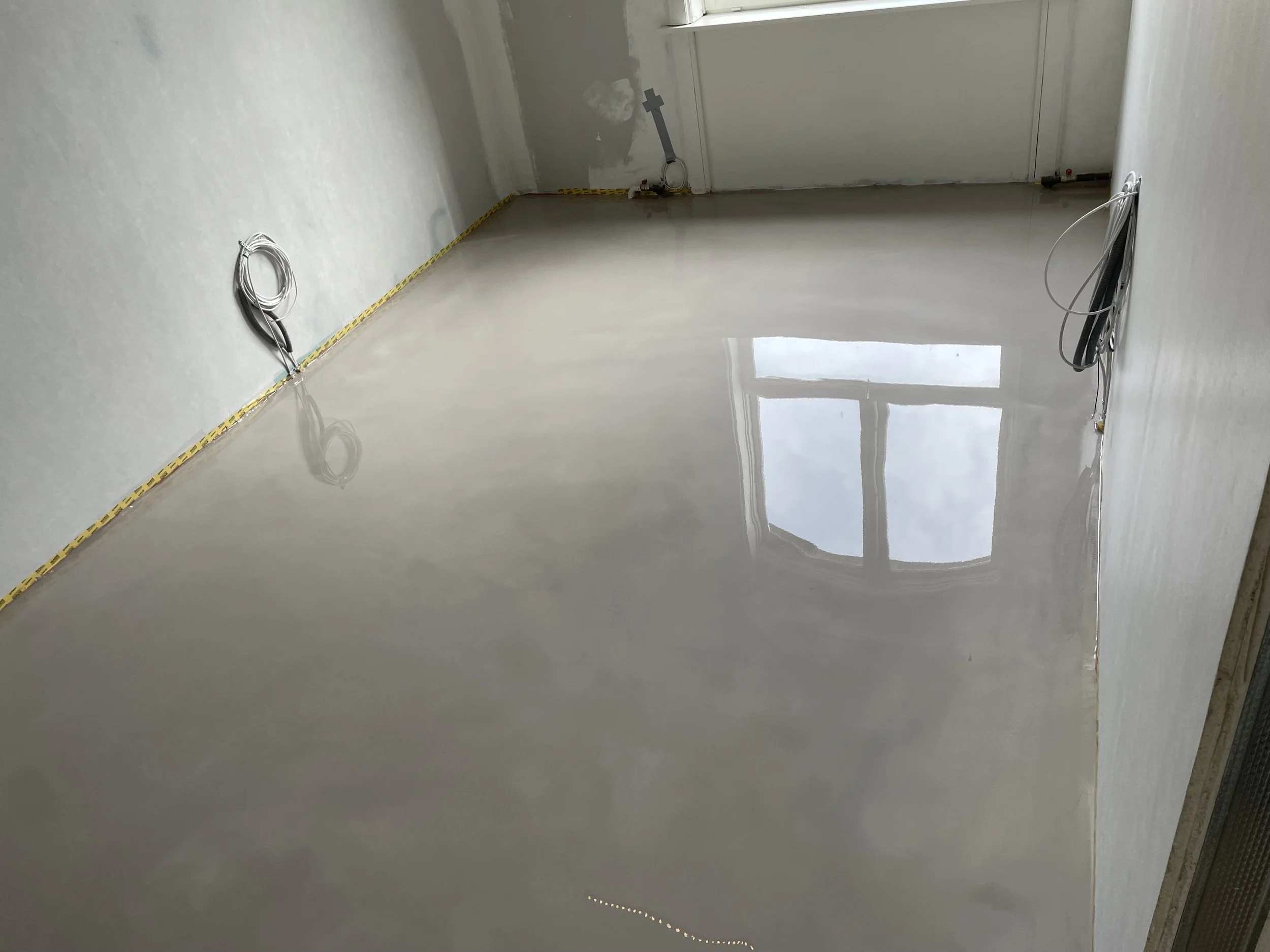 Et tomt rum under renovering med blankt gulv, vægge uden stuemaling, og elektriske ledninger, der er klar til installation.