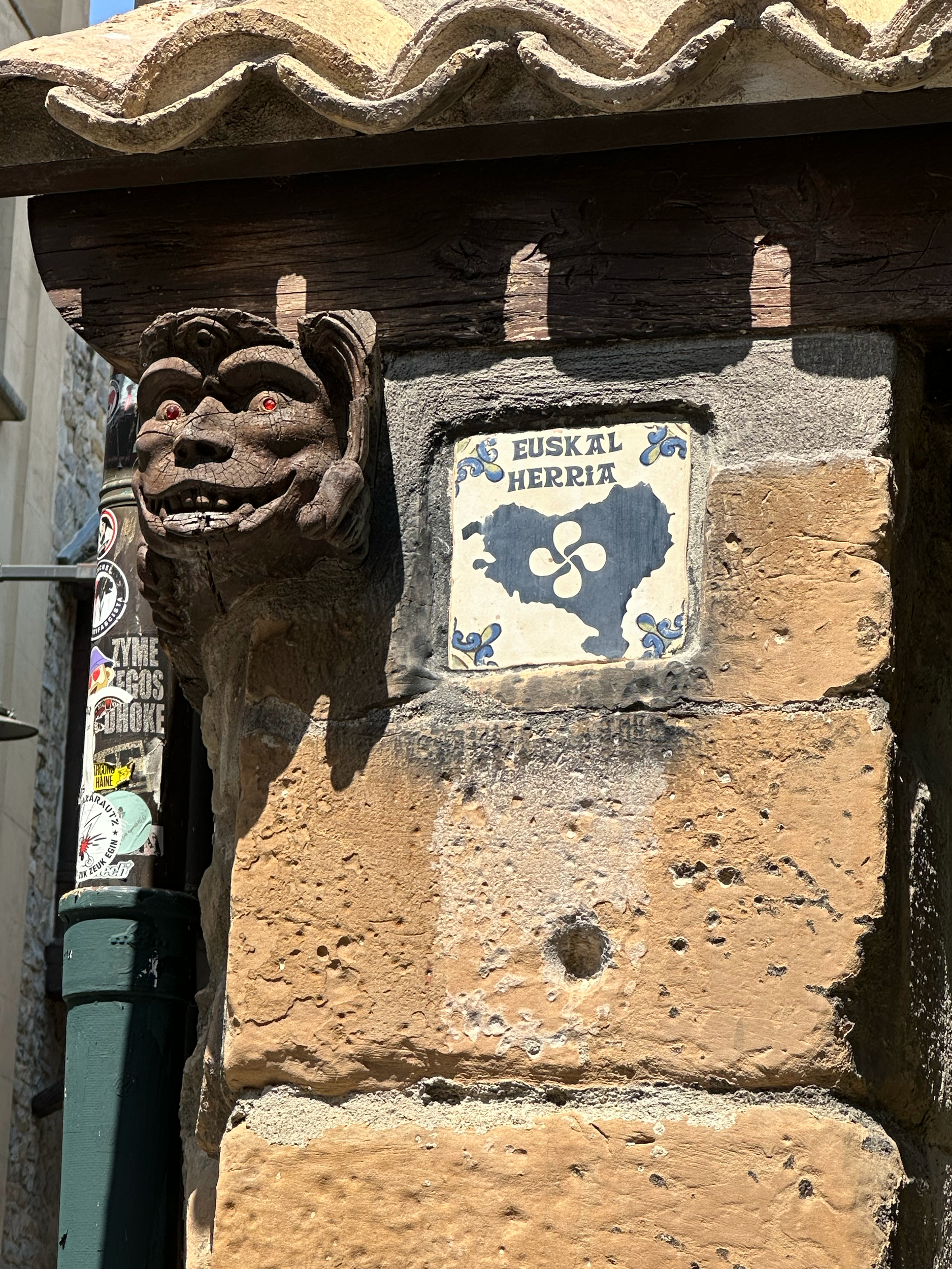 Gargoyle carved into the wood of the building and a tile supporting the "Pais Basque" or Basque country with the Basque cross in the center (looks like 4 commas forming a pinwheel).