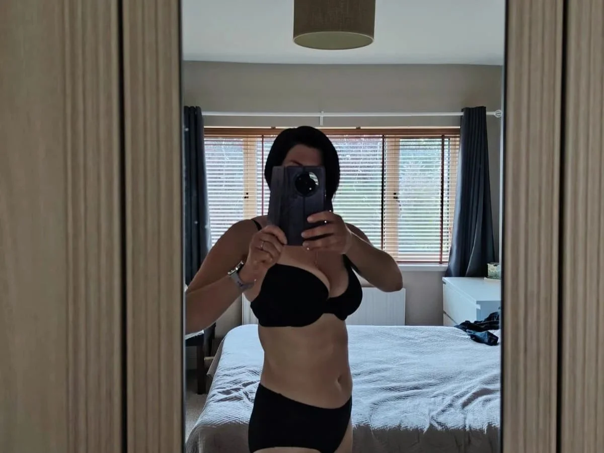 Woman taking a mirror selfie in a bedroom, wearing black underwear.