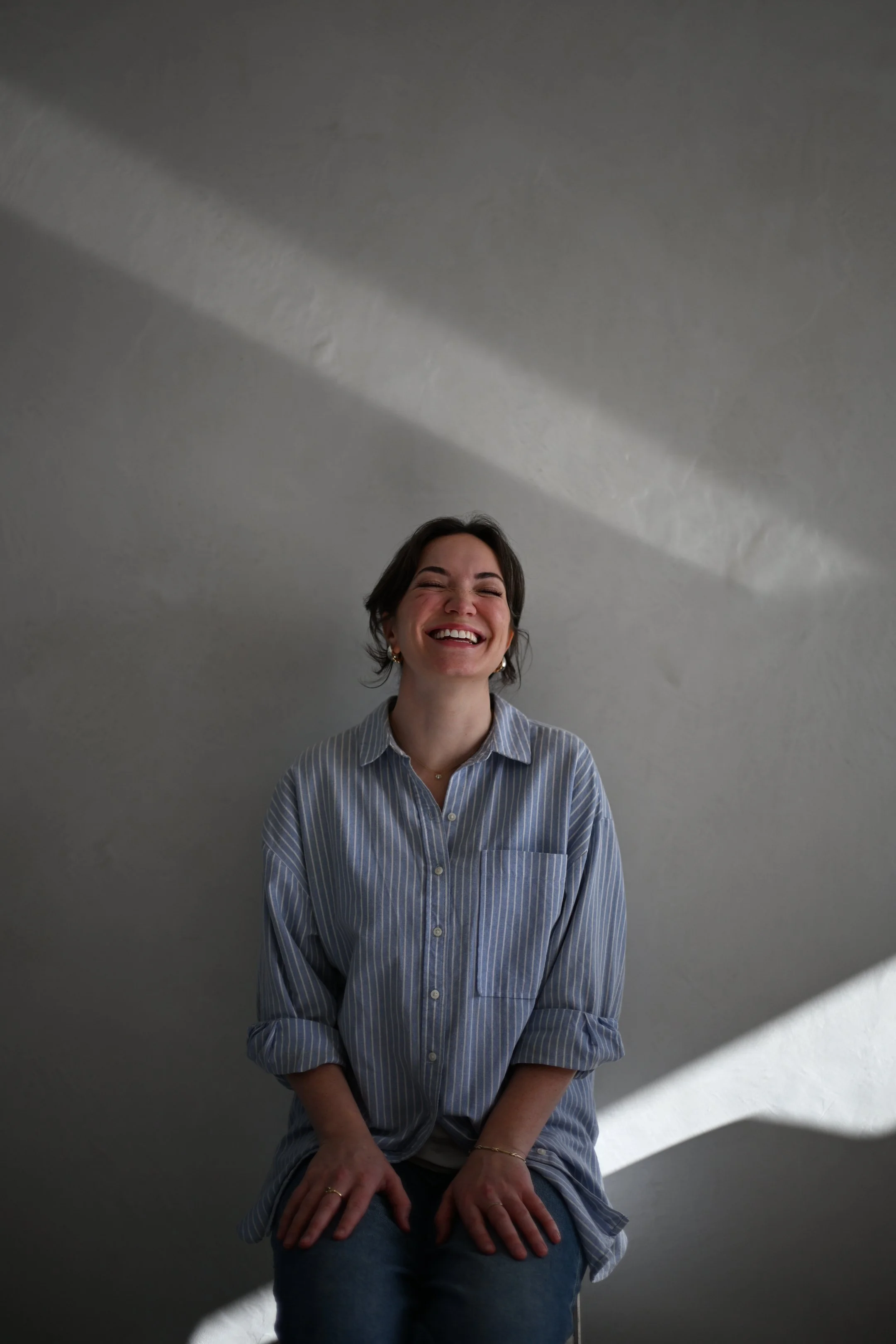A researcher with short dark hair and a big smile, wearing a blue and white striped shirt, sitting against a plain wall.