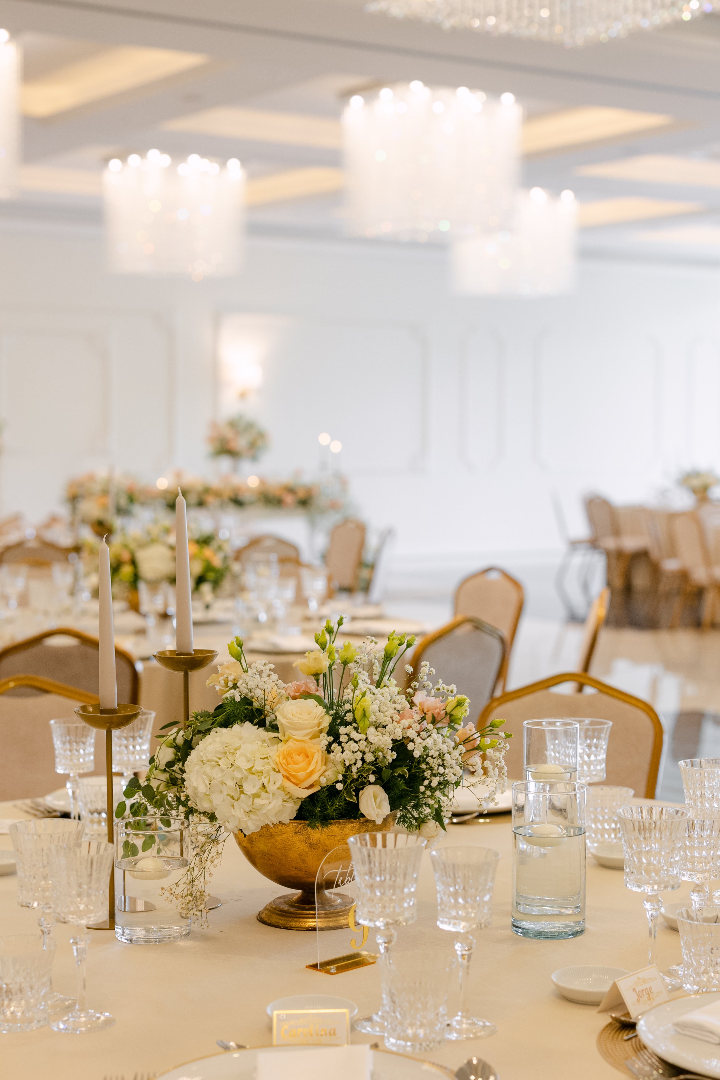 Mesa decorada com flores, velas e copos de cristal em um evento elegante, com iluminação suave e ambiente sofisticado.