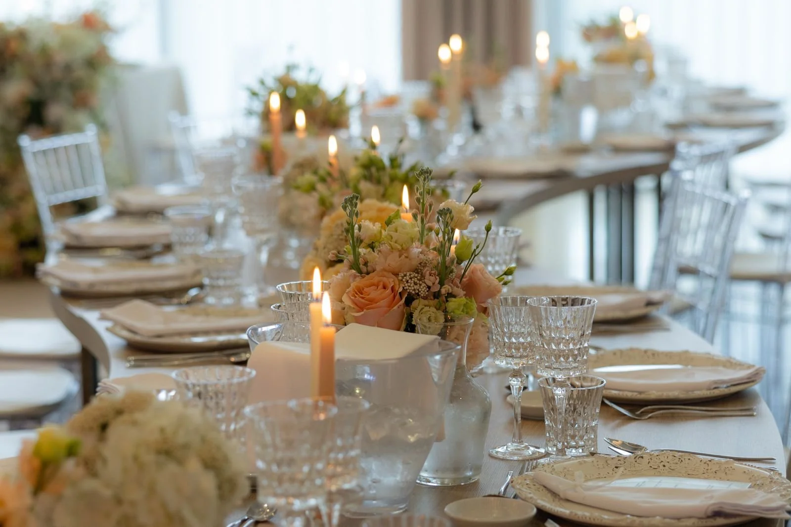 Mesa decorada para evento com velas acesas, flores e pratos dispostos com porcelana elegante.