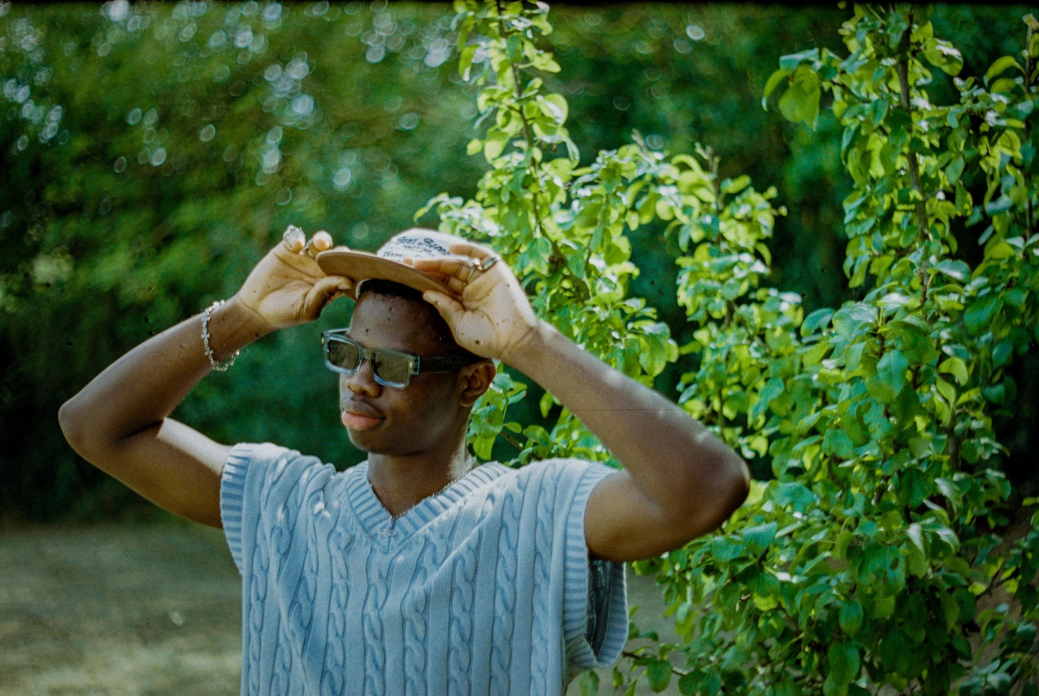 A person wearing glasses and a white striped shirt holds a small device to their forehead outdoors amidst green bushes.
