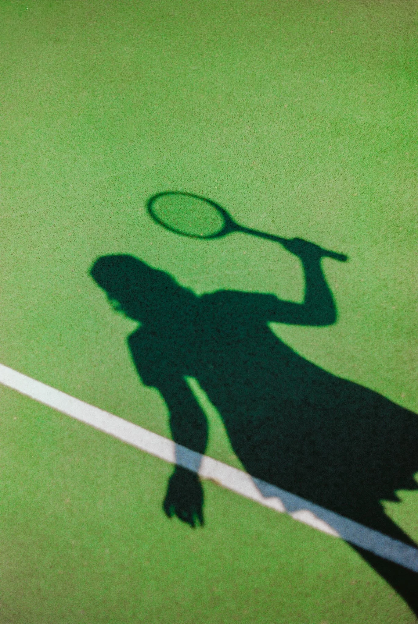 Shadow of a person holding a tennis racket on a green tennis court