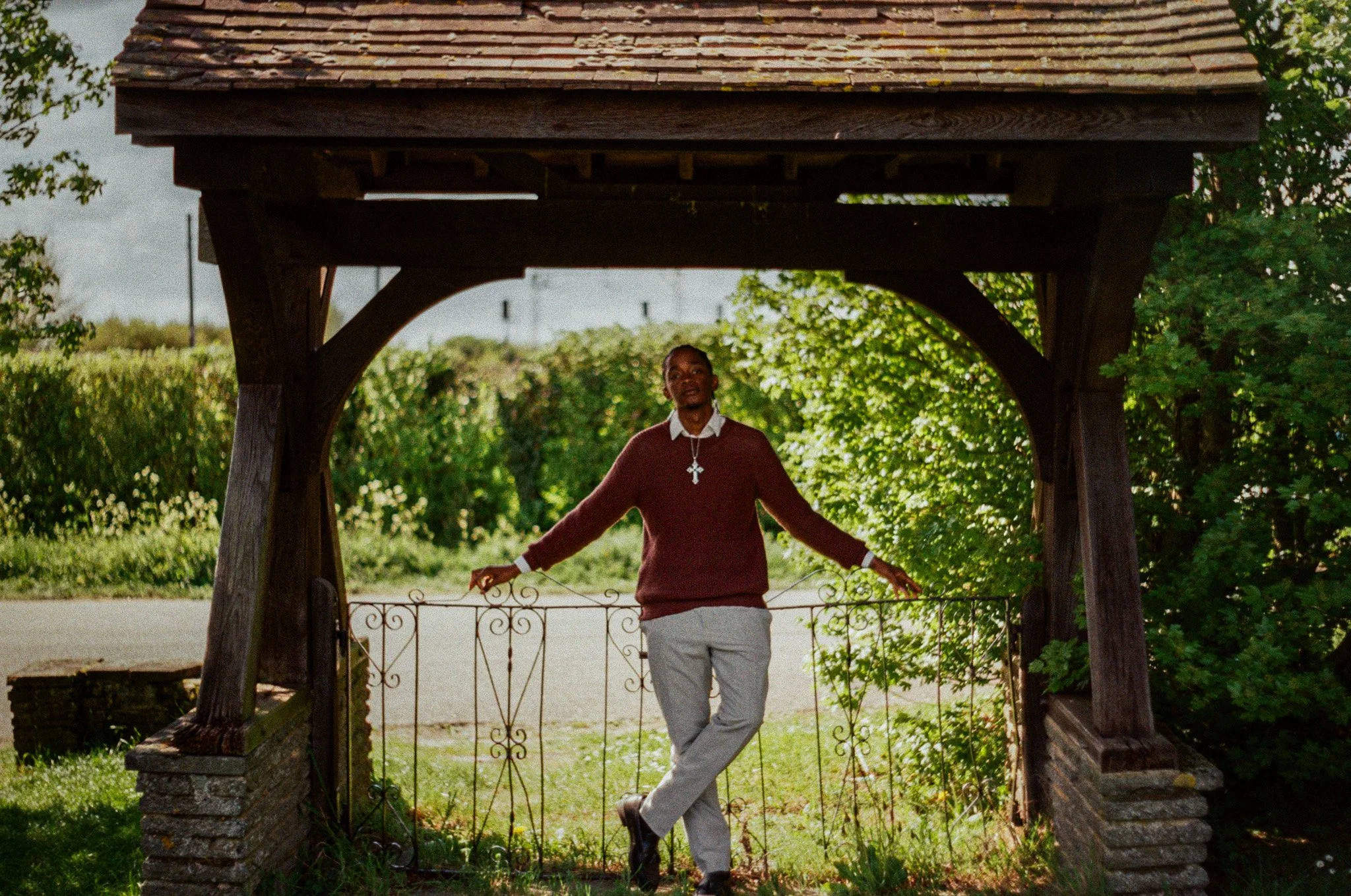 A man standing under a wooden gazebo holding a bicycle, surrounded by trees and greenery.