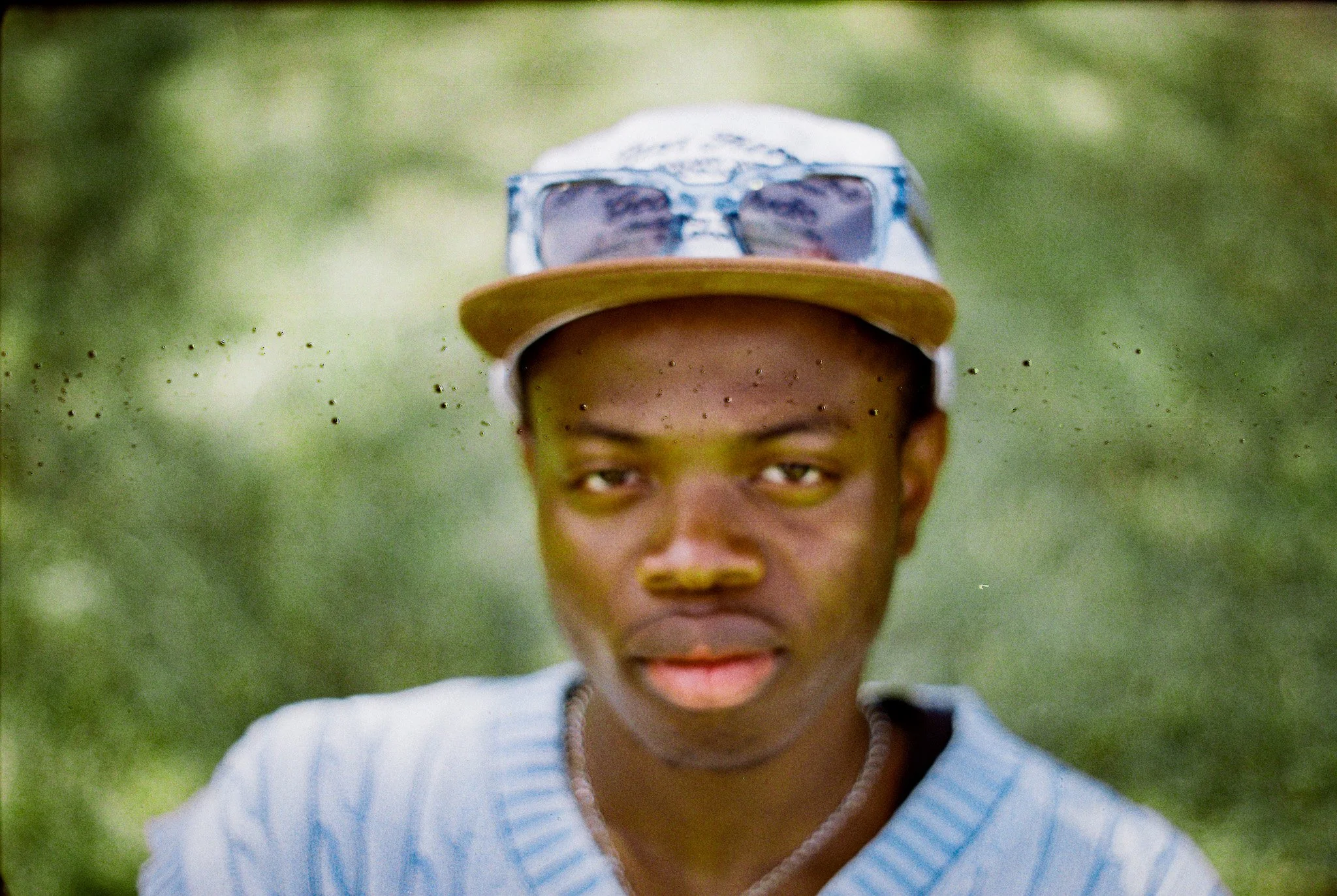 A child wearing sunglasses and a cap, outdoors in a grassy area, smiling.