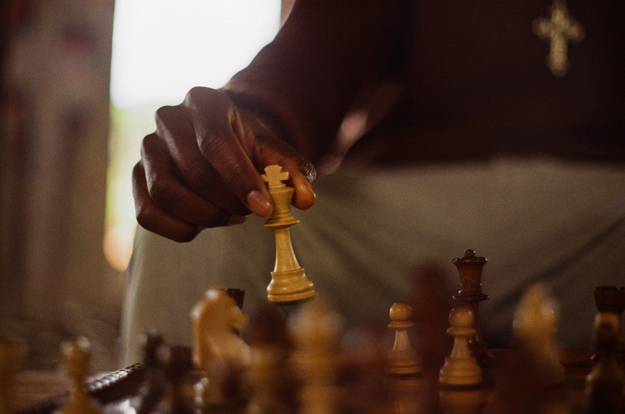 Close-up of a person making a move in a chess game, hand holding a white knight piece on a chessboard.