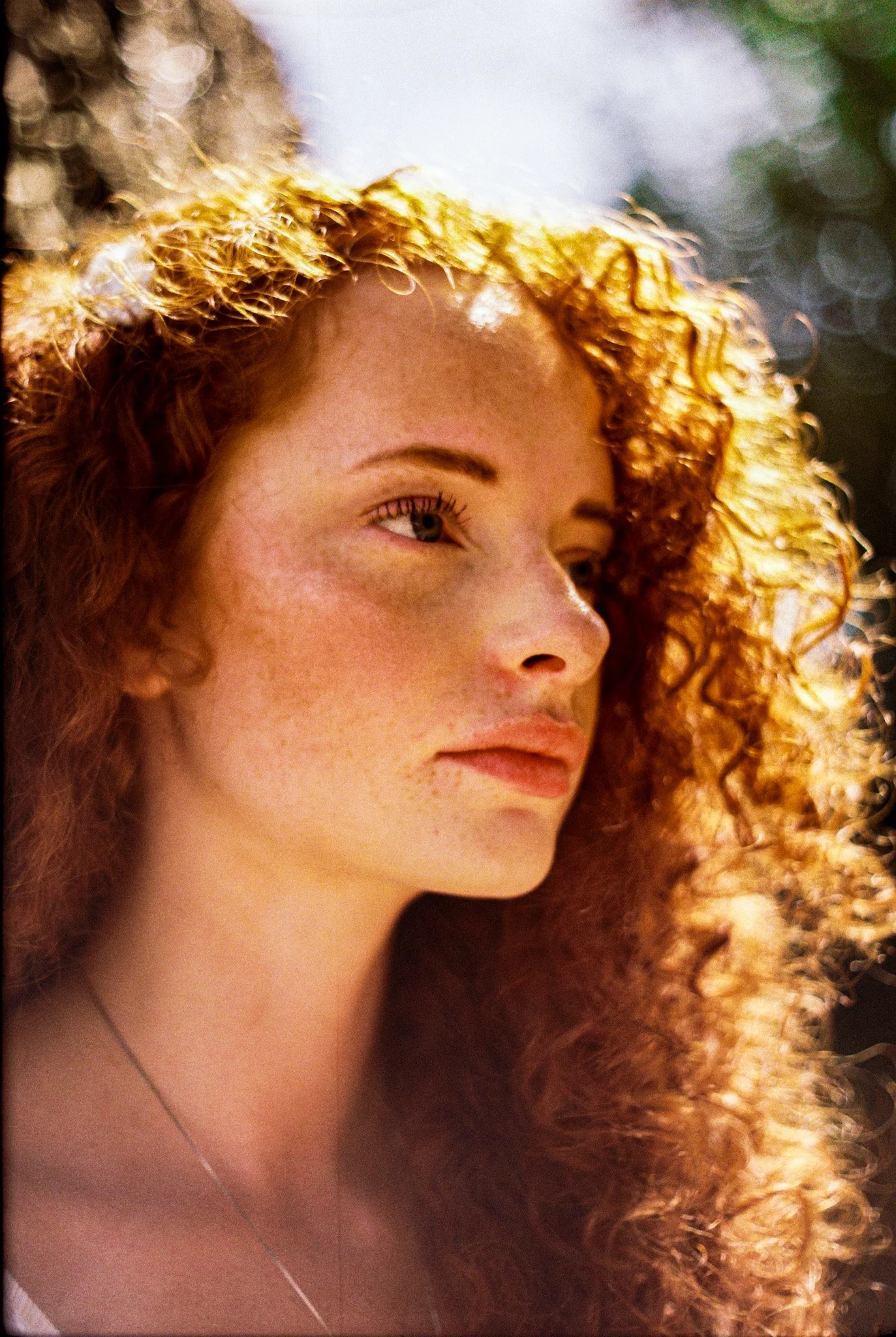 Close-up of a woman with curly red hair and light skin, looking to the side.