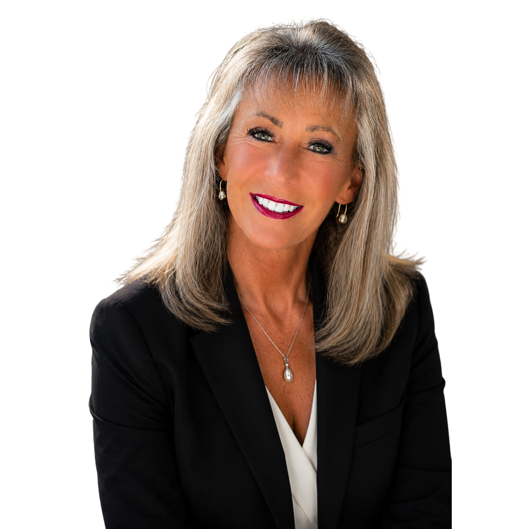 A smiling middle-aged woman with blonde hair styled in loose waves, wearing a black blazer over a white top, gold drop earrings, and a pearl pendant necklace.