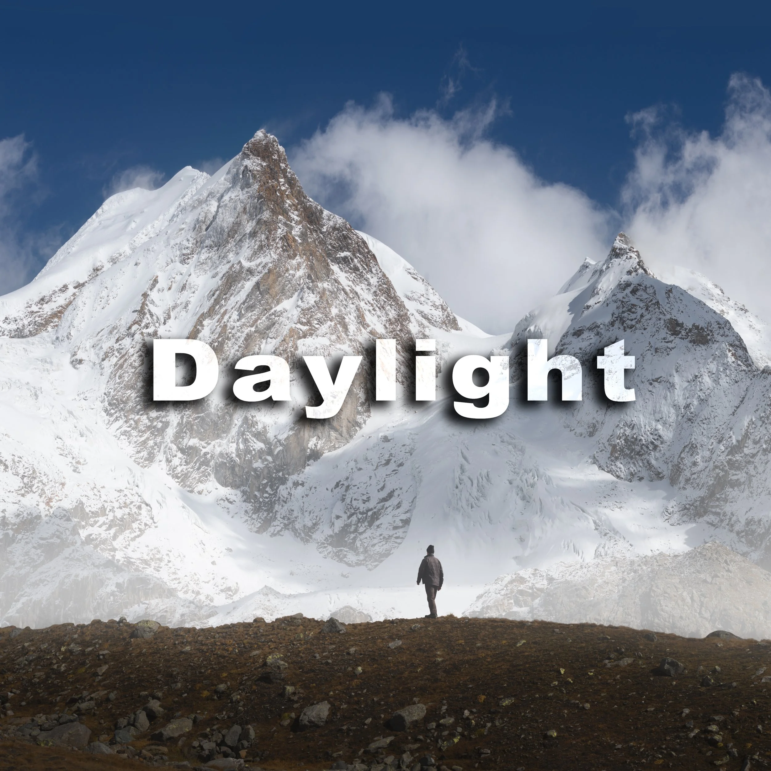 A person standing on rocky ground at the base of a snow-covered mountain under a partly cloudy sky.
