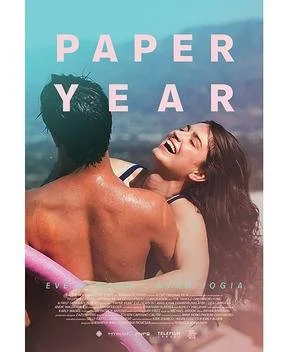 A young couple smiling and embracing at the beach, with the words 'PAPER YEAR' in large letters across the top.