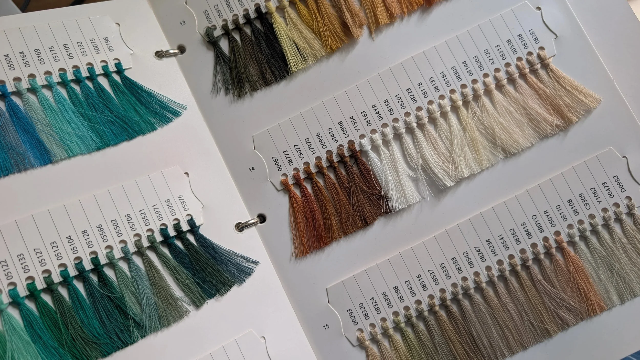 Farbfadenmusterkarte mit verschiedenen Farben, darunter Blau, Schwarz, Beige, Weiß und Braun.