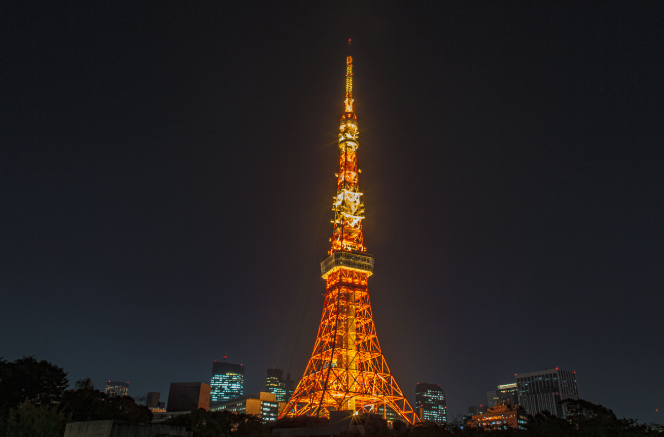 Tokyo Tower illuminated at night against a dark sky, with city buildings at the base.