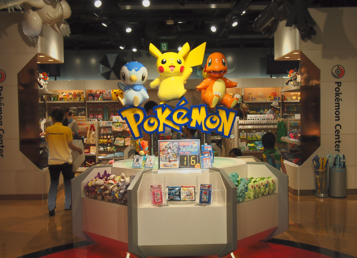 Pokémon Center retail store display with large Pokémon statues of Pikachu, Squirtle, and Charmander, surrounded by shelves of Pokémon merchandise and plush toys.