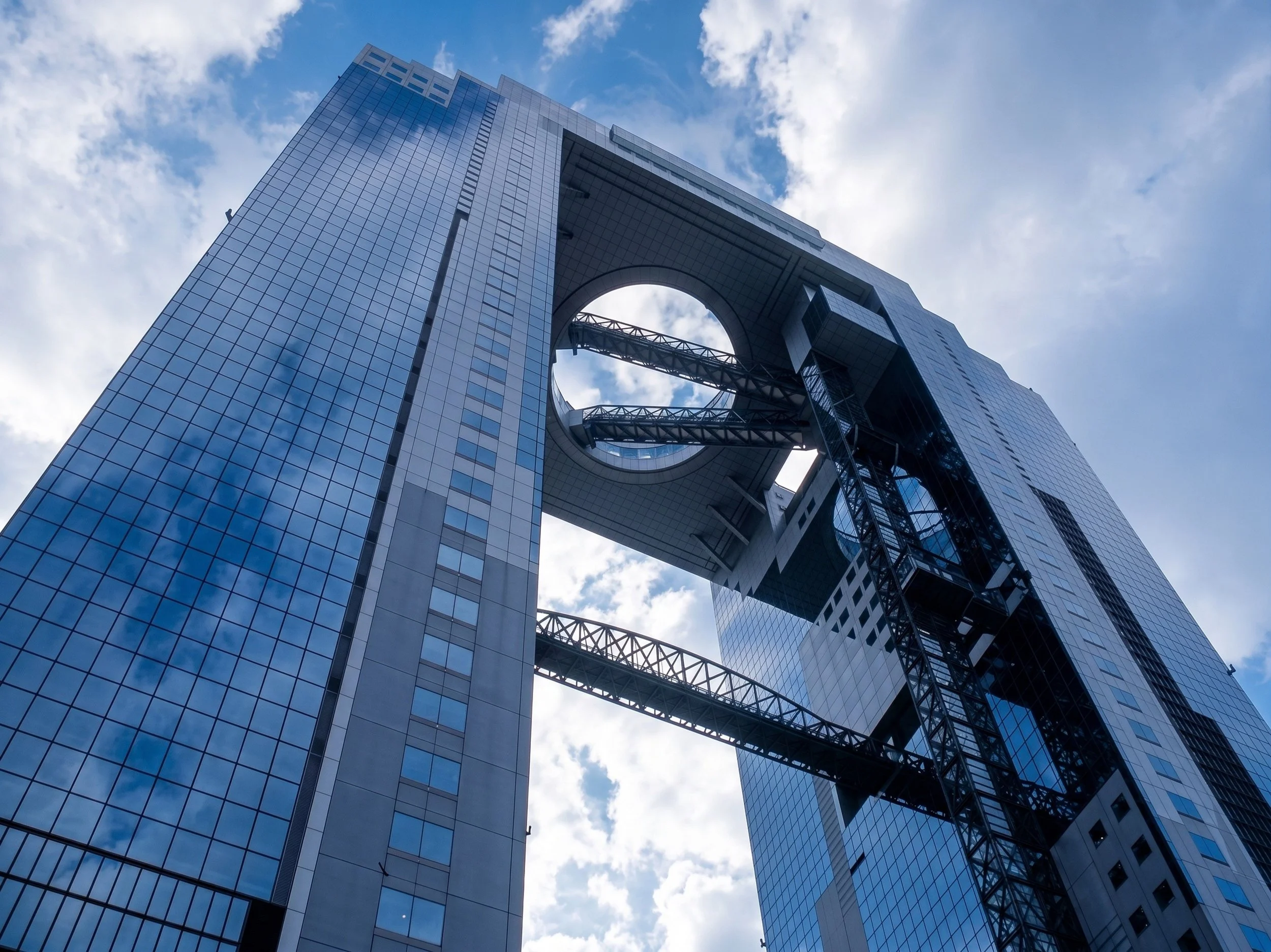 A modern skyscraper with a large circular opening in the middle, featuring glass exterior walls reflecting the sky and clouds.