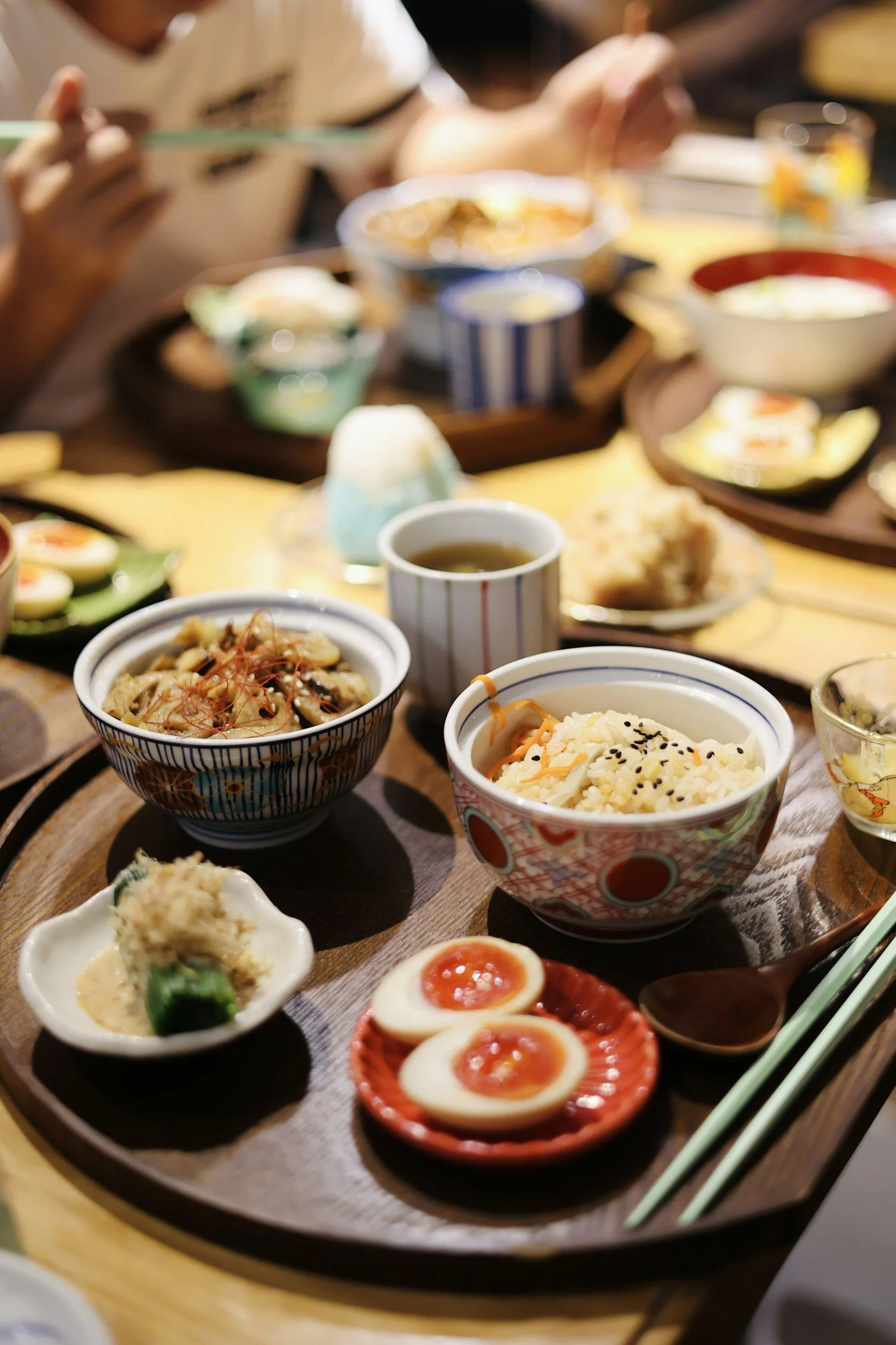 Assorted Japanese dishes on a round wooden tray, including ramen, rice, soft-boiled eggs, and various side dishes.