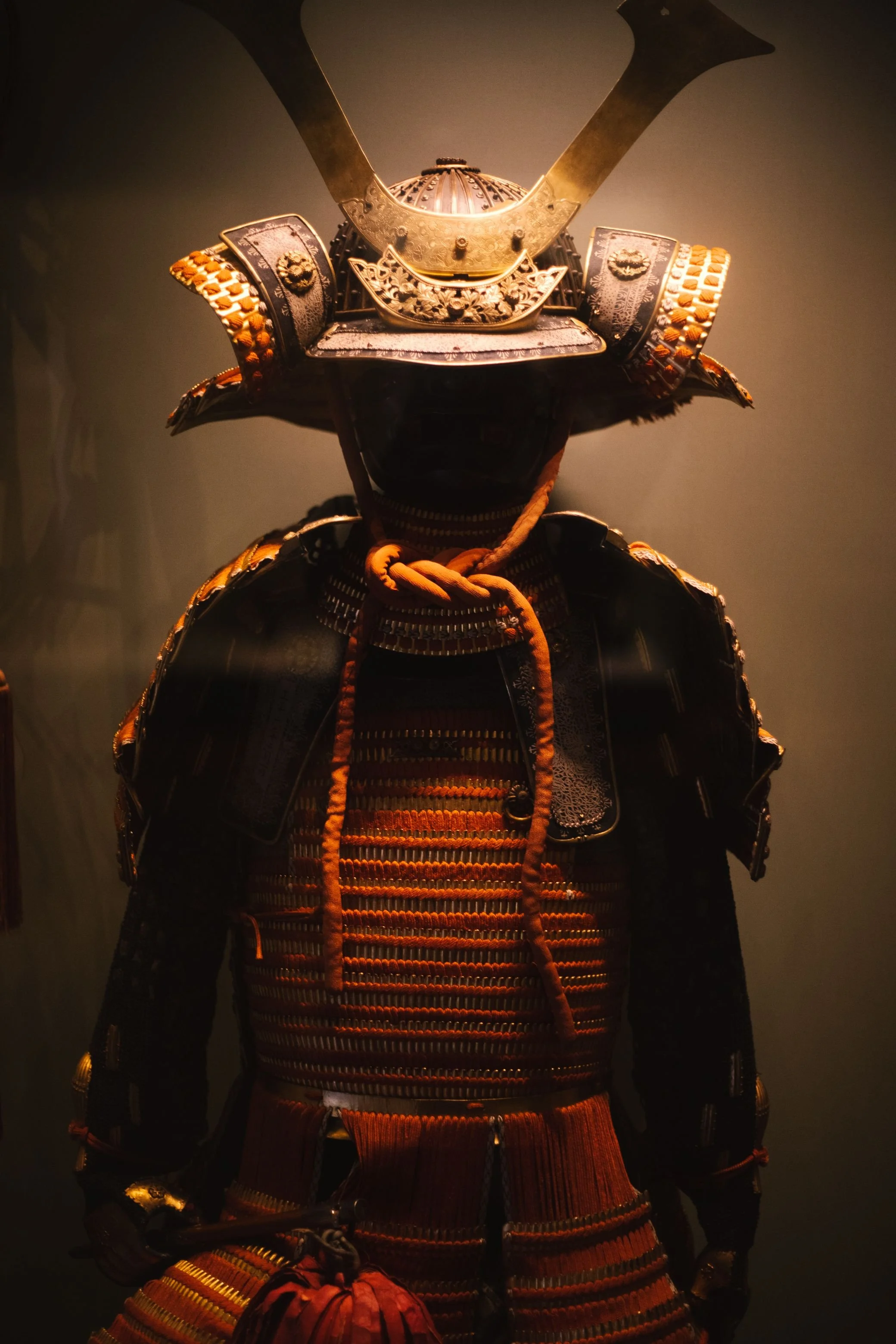 A traditional samurai armor suit with a helmet featuring a large crest, intricate metalwork, and decorative elements, displayed against a dark background.