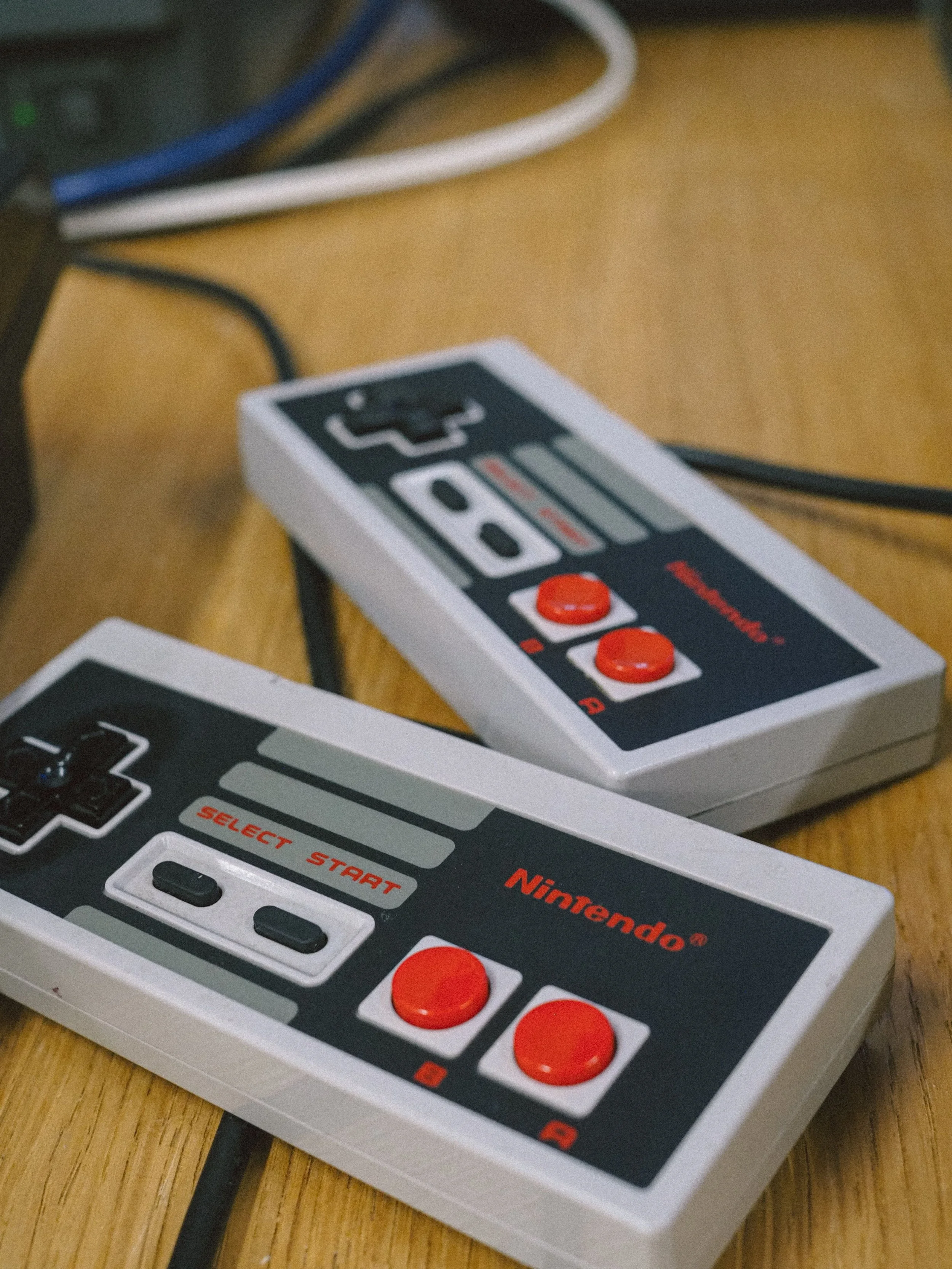 Close-up of a Nintendo controller model resembling the Nintendo Entertainment System (NES), placed on a wooden surface with some cables in the background.