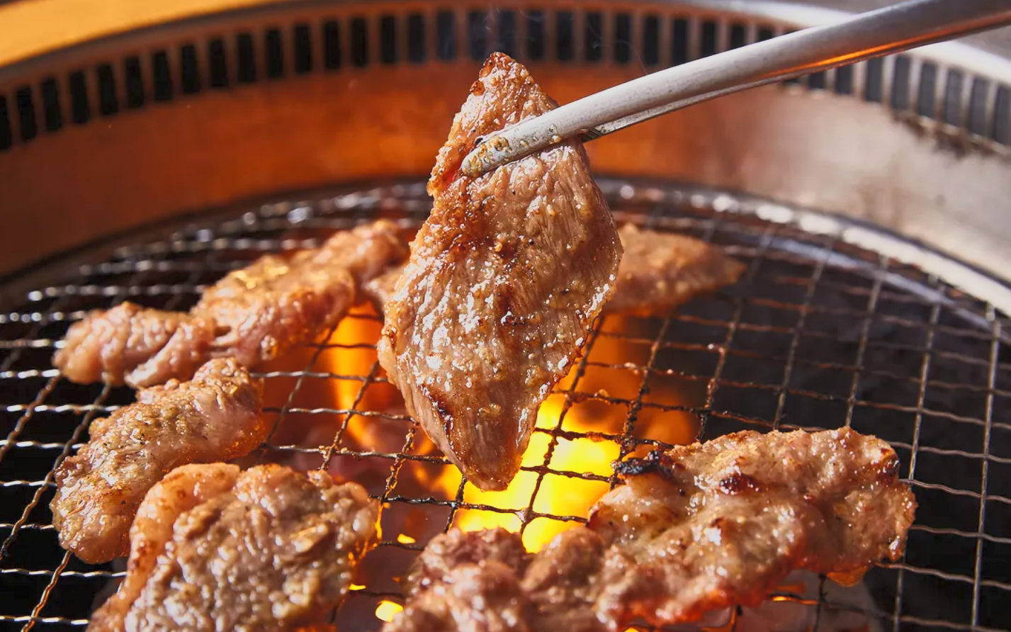 Slices of beef grilling on a barbecue over open flame.