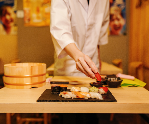 Person preparing sushi on a black sushi tray in a restaurant.