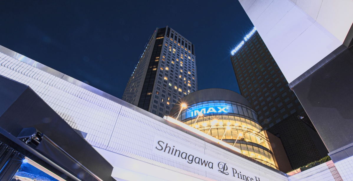 Night view of tall buildings in a city, with illuminated signs that read 'IMAX' and 'Shinagawa Prince Hotel'