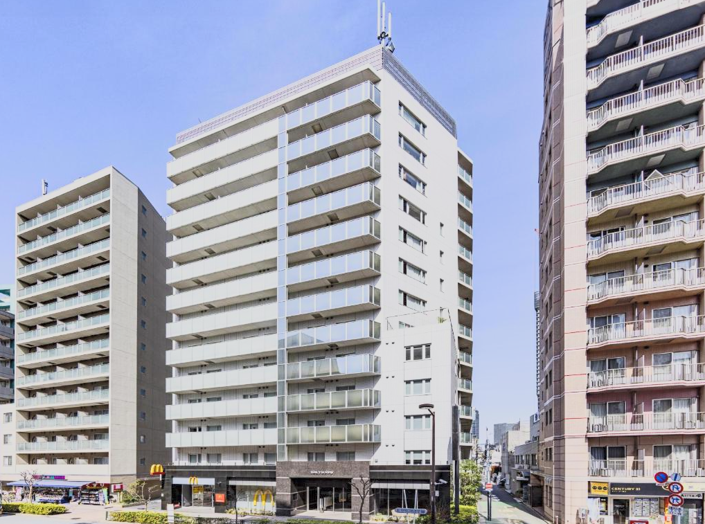 Tall modern apartment buildings with glass balconies along a city street under a blue sky.