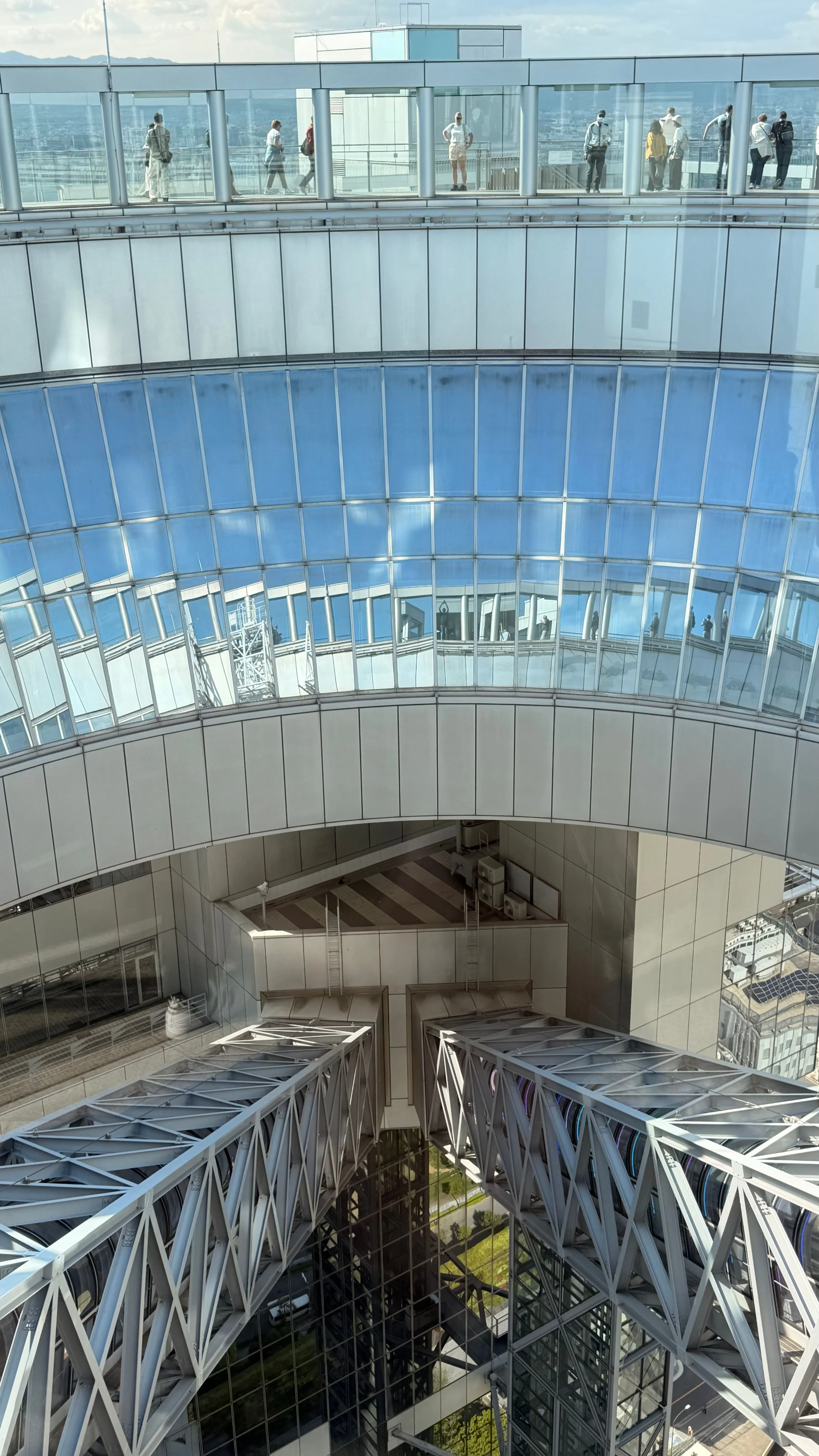 View of high-rise building interior with glass walkways and a central atrium, with people walking on the upper walkway.