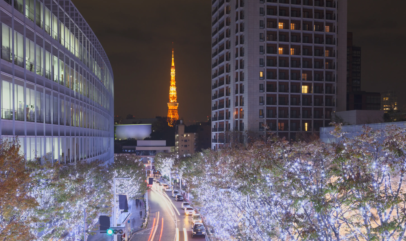 Night city street with trees decorated with white string lights, high-rise buildings on both sides, and Tokyo Tower illuminated in the background.