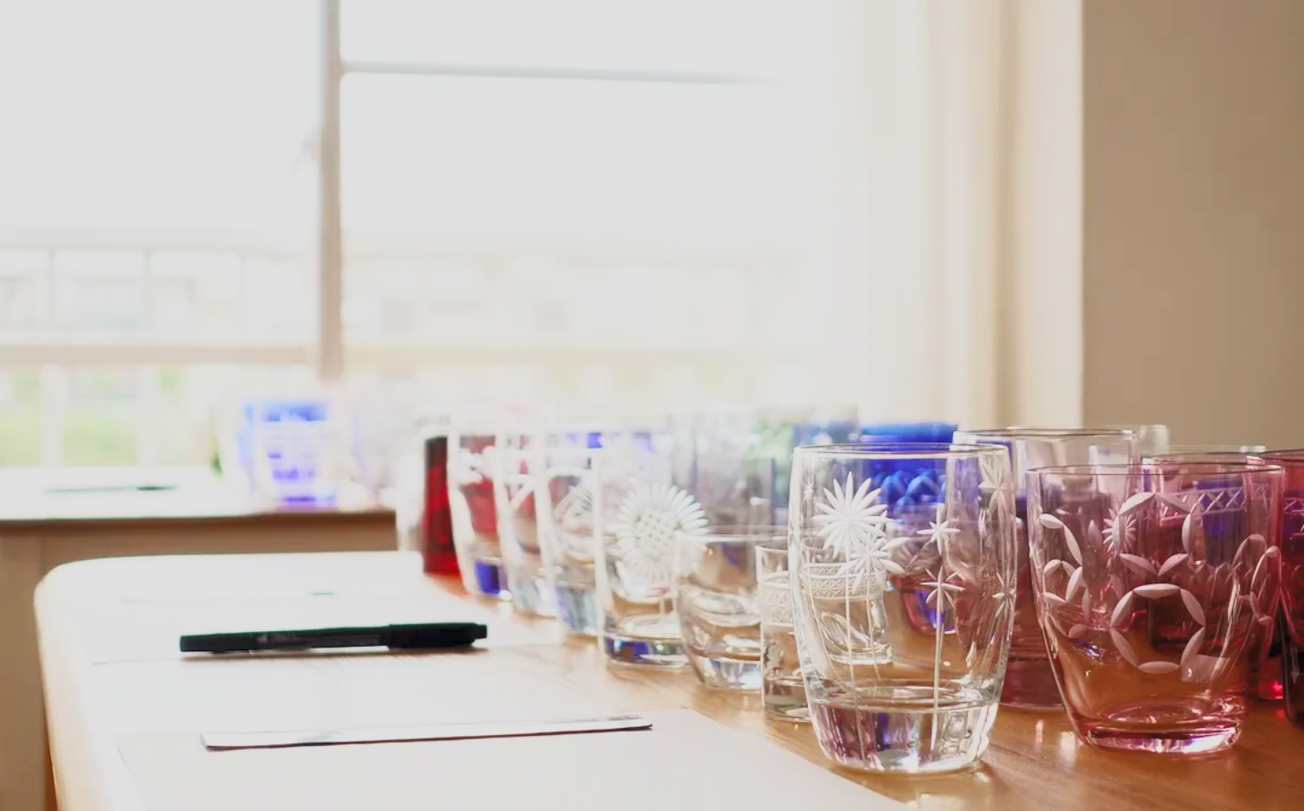 A row of colorful glass tumblers with floral engravings on a wooden table near a window.