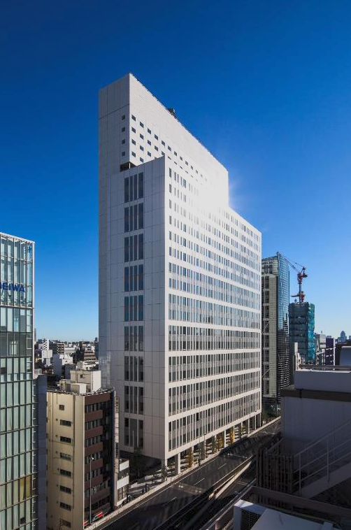 Tall modern white office building in city skyline under clear blue sky.