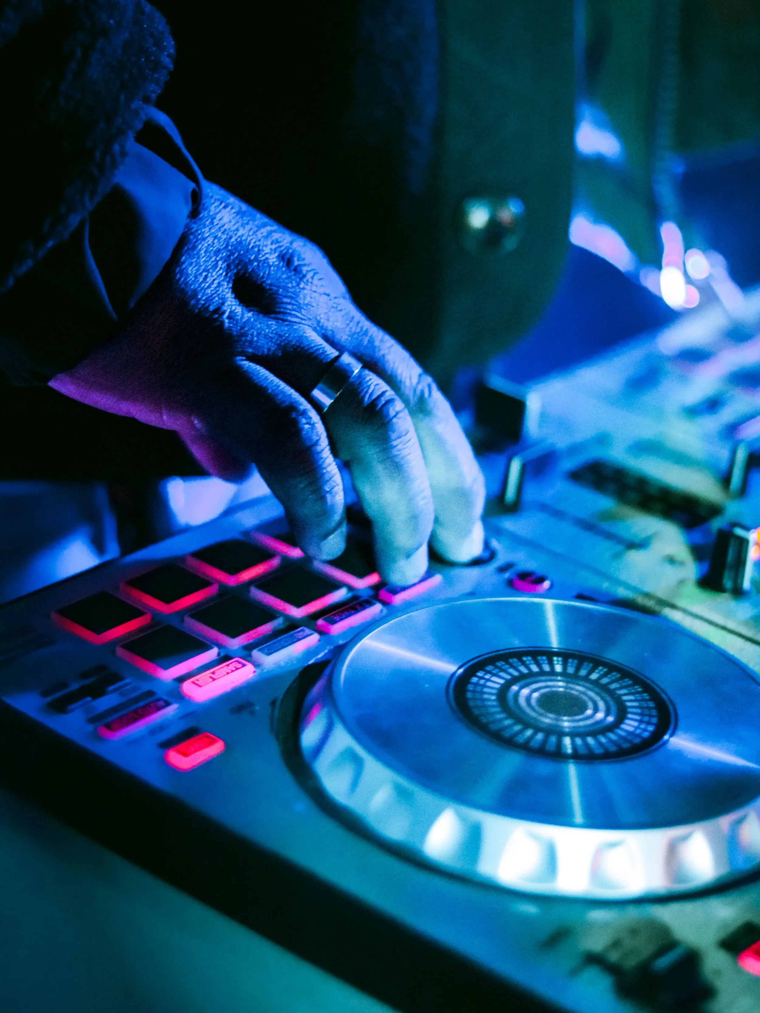 Close-up of a DJ's hand on a music mixer with colorful lights and a turntable in a nightclub setting.