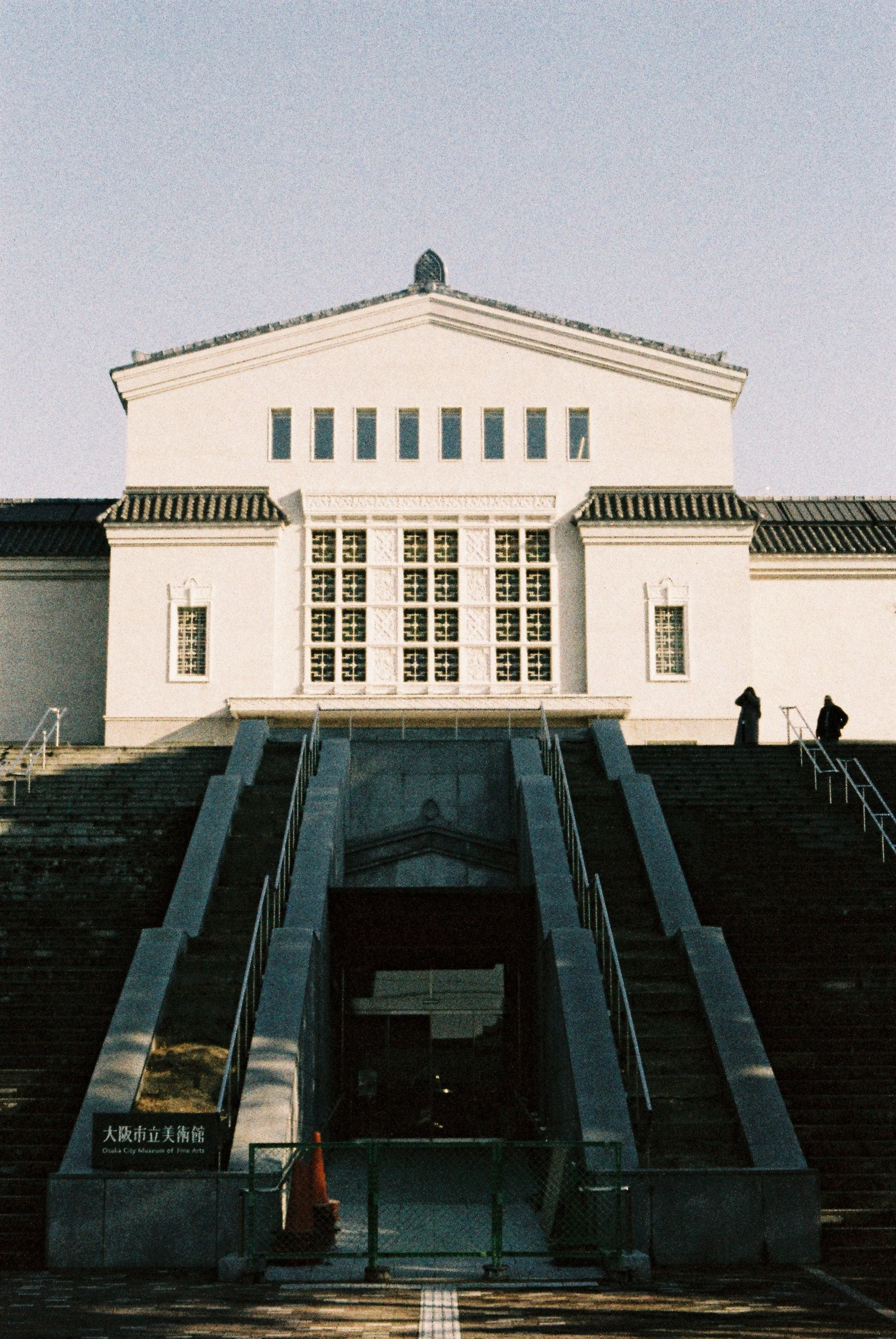 Front view of Osaka City Museum of Fine Arts, with steps leading up to the entrance, partially covered by a fence, during daylight.