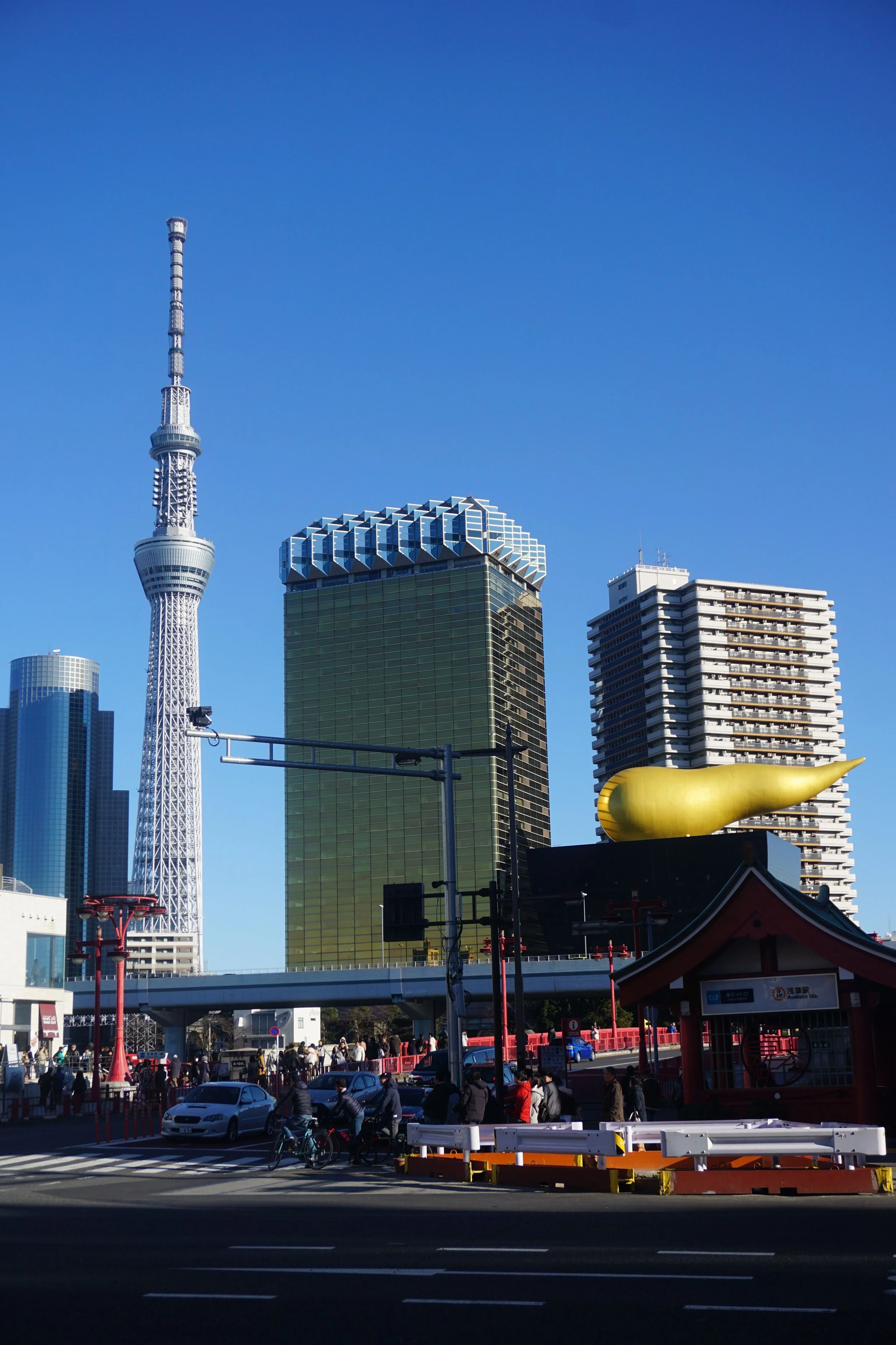 Cityscape featuring Tokyo Skytree and modern high-rise buildings, with people and cars on a busy street in Japan.