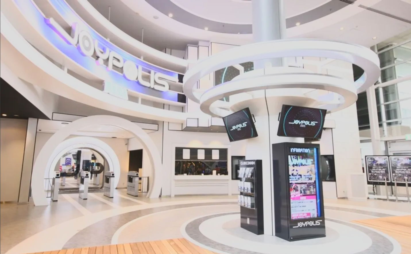 Modern shopping mall entrance with Joypolis signage, digital display screens, and white architectural arches.