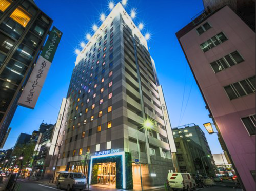 A tall, modern office building illuminated at night in an urban area, with bright lights and clear blue sky.