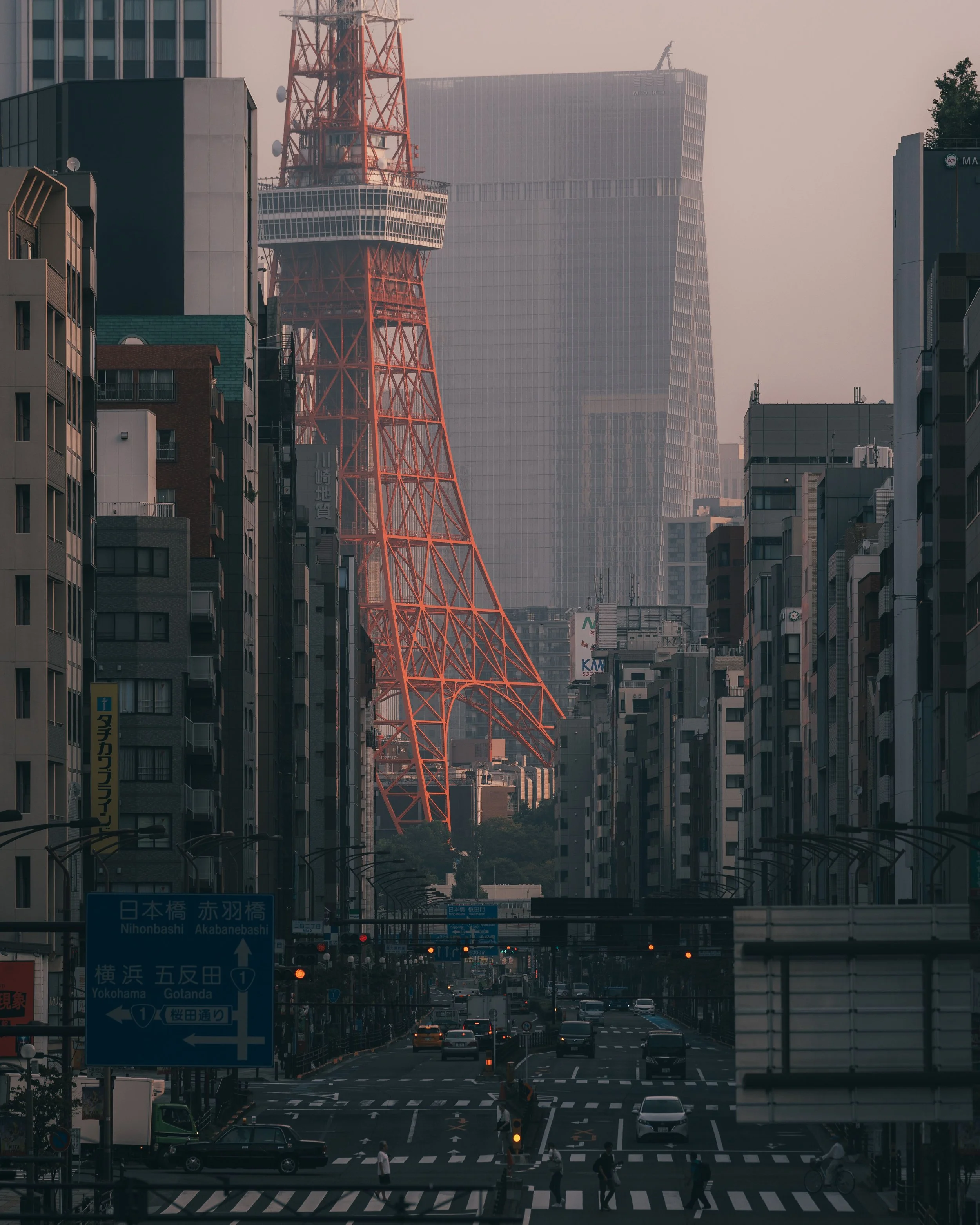 City street scene with traffic and pedestrians, with Tokyo Tower and modern high-rise buildings in the background.