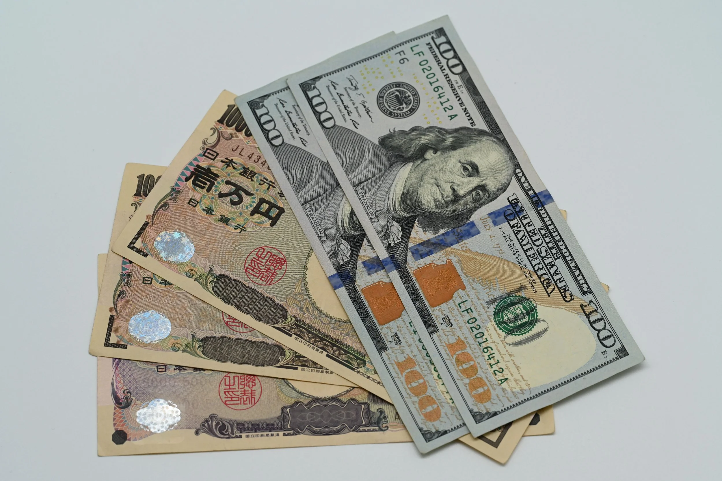 A collection of US and Japanese banknotes, including a $100 US bill and multiple ¥10,000 Japanese yen notes, laid on a plain surface.